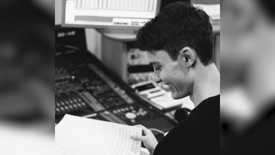 Black and white photo of male alumnus in a music studio, looking at sheet music.